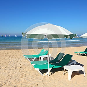 Sandy beach with sun umbrella and green lounges