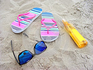 Sandy beach with sunglasses, flip-flops and suncare milk