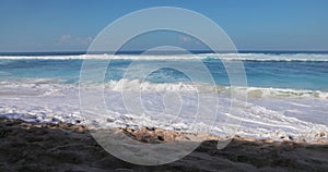 Sandy beach on sunny day with blue ocean waves in tropics