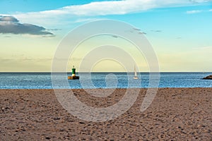 Sandy beach at sunset with small sailboats sailing and buoys in the sea, Gijon, Asturias.