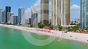 Sandy beach with tourists relaxing under red sun umbrellas along ocean shore at Sunny Isles Beach. Exquisite resort in