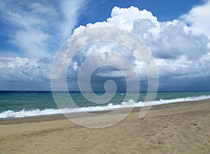 Sandy beach on a warm summer day, turquoise sea with glebe waves and large rain clouds over the sea, Italy, Calabria