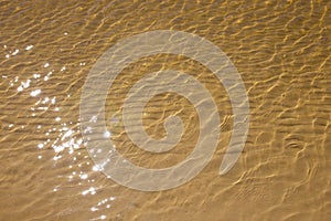 The sandy bottom is yellow, yellow sand under water. The sun rays are reflected on surface of the water. Texture of the