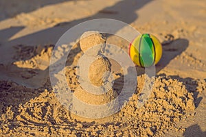 Sandy christmas snowman in red santa hat and sunglasses at sunny beach. Holiday concept for New Years Cards