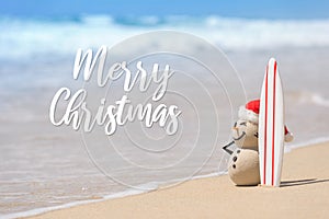 Sandy Christmas Snowman is standing on beautiful beach with a surf board