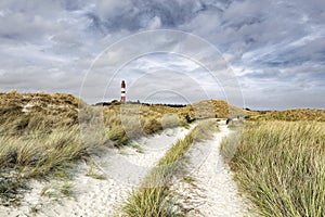 Sandy dirt road through coastal landscape. Bicycles standing at bike parking place. Red and white striped naval lighthouse in