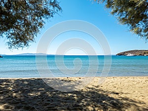 Sandy empty beach with tree shadow, moored yacht in calm sea at Greek islands, Cyclades Greece