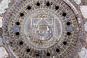 Sandy manhole cover with the coat of arms of the city ratzeburg in a cobblestone street  high angle view from above