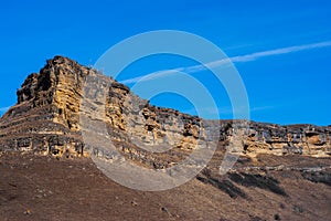 Sandy mountain with a sharp cliff and a small amount of vegetation against the blue sky