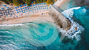 Sandy paradise: Umbrella-dotted shoreline, waves seen from above.