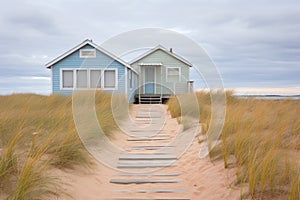 a sandy path surrounded by beach grass leading up to a pastel blue beachside cottage