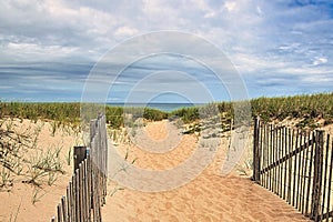 Sandy pathway through dunes to an ocean beach on a cloudy summer day.