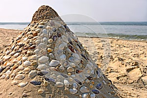 Sandy pyramid with shells on a sea beach