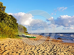 On the sandy shore of the sea lies a small wooden boat. Cloudy warm summer day on the Batian Sea