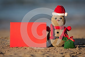 Sandy snowman with blank card at tropical beach.