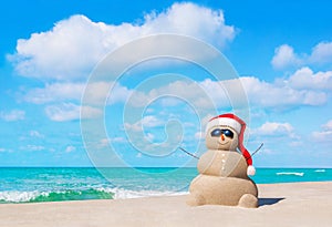 Sandy Snowman in Christmas Santa hat and sunglasses at beach