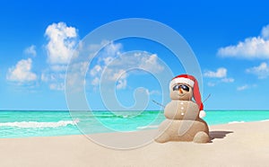Sandy snowman in Christmas Santa hat and sunglasses at beach