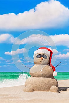 Sandy snowman in red Santa hat and sunglasses at tropical ocean beach