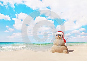Sandy snowman in santa hat on sea beach. New Years and Christmas
