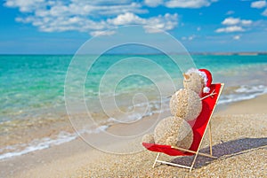 Sandy snowman in santa hat sunbathing in beach lounge.