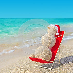Sandy snowman in santa hat sunbathing in beach lounge.