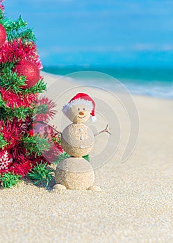 Sandy Snowman in Santa hat under decorated Christmas Tree at beach