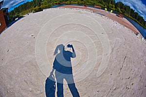 The sandy surface of the beach games area is formed by bright daylight on which the shadow of the silhouette of the photographer