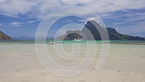 Sandy tropical beach of El Nido bay with fishing banca boats floating in blue lagoon in a distance. Palawan island