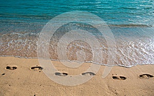 Sandy tropical beach with sea waves. Foot steps on the shore. Footp rints in the sand at sunset.