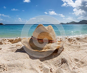 Sandy tropical beach, straw hat beach accessories and blue sea.