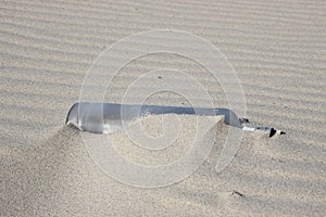 Sandy waves and a half hidden bottle in a sand beach