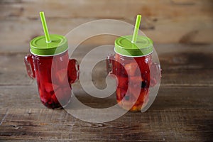 Sangria of fresh berries and citrus fruits in a glass with a drinking straw on a table made of natural wood. Fresh summer cocktail