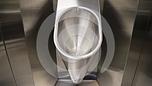 Sanitary metal urinal, toilet bowl in public bathroom with hygienic automatic water saving electronic flush.