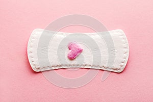 Sanitary pad with pink woolen heart as blood drop on pastel rose background, menstruation cycle, intimate hygiene