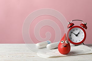 Sanitary pads with feather, decorative blood drop and alarm clock on wooden table