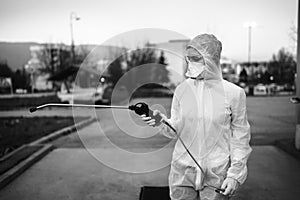 Sanitation service worker spraying disinfectant with a spray gun in hazmat suit,N95 mask and protective gear.Private protective