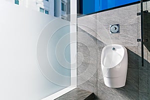 Sanitation white ceramic urinal in the men`s bathroom with hygienic automatic water-saving electronic flusher.