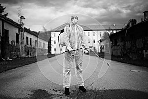 Sanitation worker in hazmat protection suit  and N95 mask with chemical decontamination sprayer tank.Disinfecting streets and photo