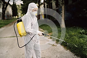 Sanitation worker in hazmat protection suit  and N95 mask with chemical decontamination sprayer tank.Disinfecting streets and