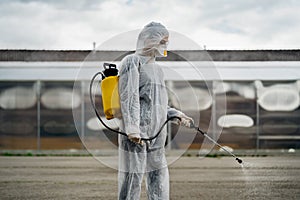 Sanitation worker in hazmat protection suit and N95 mask with chemical decontamination sprayer tank.Disinfecting streets and