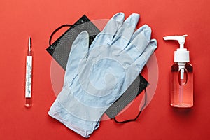 Sanitizer bottle, Medical surgical mask, lab gloves and thermometer - Virus protection equipment on red background