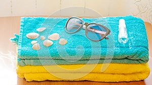 A sanitizer bottle, sunglasses and shells lie on a blue towel. The concept of a summer vacation in a new reality.