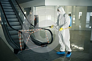 Sanitizing worker disinfects the escalator with a spray at the empty shopping mall to prevent the covid-19 spread in public places