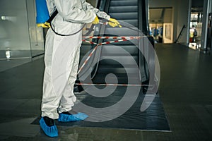 Sanitizing worker disinfects the escalator with a spray at the empty shopping mall to prevent the covid-19 spread in public places