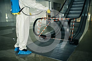 Sanitizing worker disinfects the escalator with a spray at the empty shopping mall to prevent the covid-19 spread in public places