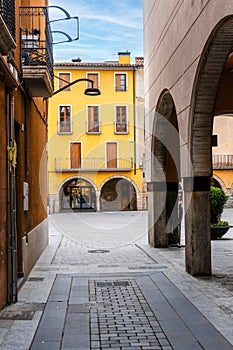 Sant Joan de les Abadesses, Spain. A narrow alleyway with a yellow building and a white archway. The archway is open and the