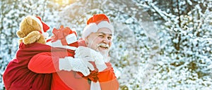 Santa carrying bag of gifts against snow scene. Winter Christmas greeting card. Santa Claus pulling huge bag of gifts on