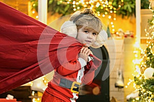 Santa child. Santa helper holding a red bag with presents. Merry christmas and happy new year. Surprised Little Santa in