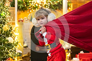 Santa child. Santa helper holding a red bag with presents. Merry christmas and happy new year. Surprised Little Santa in