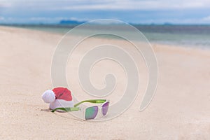 Santa Christmas hat with sunglasses in sand on a tropical beach. Holiday tropic summer concept